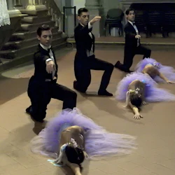 Tre dansare i smoking knäböjer med utsträckta armar; tre ballerinor i lila tutus ligger på golvet och sträcker sig framåt.