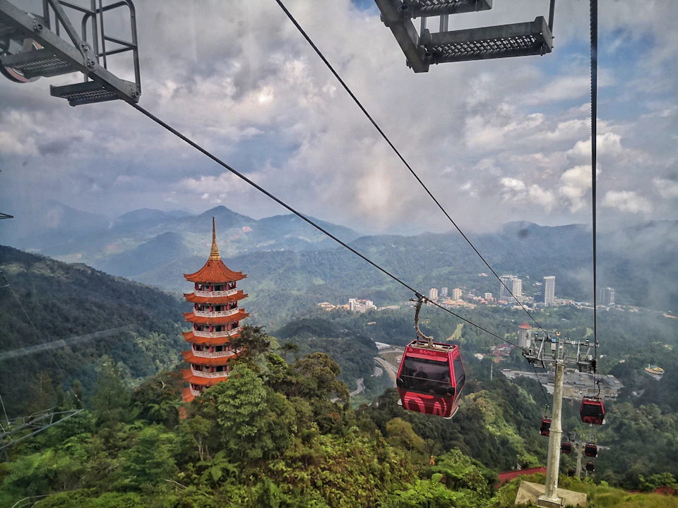Cable cars traveling over lush green hills with a red pagoda in the foreground and a cityscape in the background.
