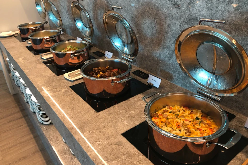 A buffet counter with four copper pots containing various dishes, placed on a stone countertop with labels for each dish.