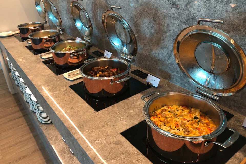 A buffet counter with four copper pots containing various dishes, placed on a stone countertop with labels for each dish.