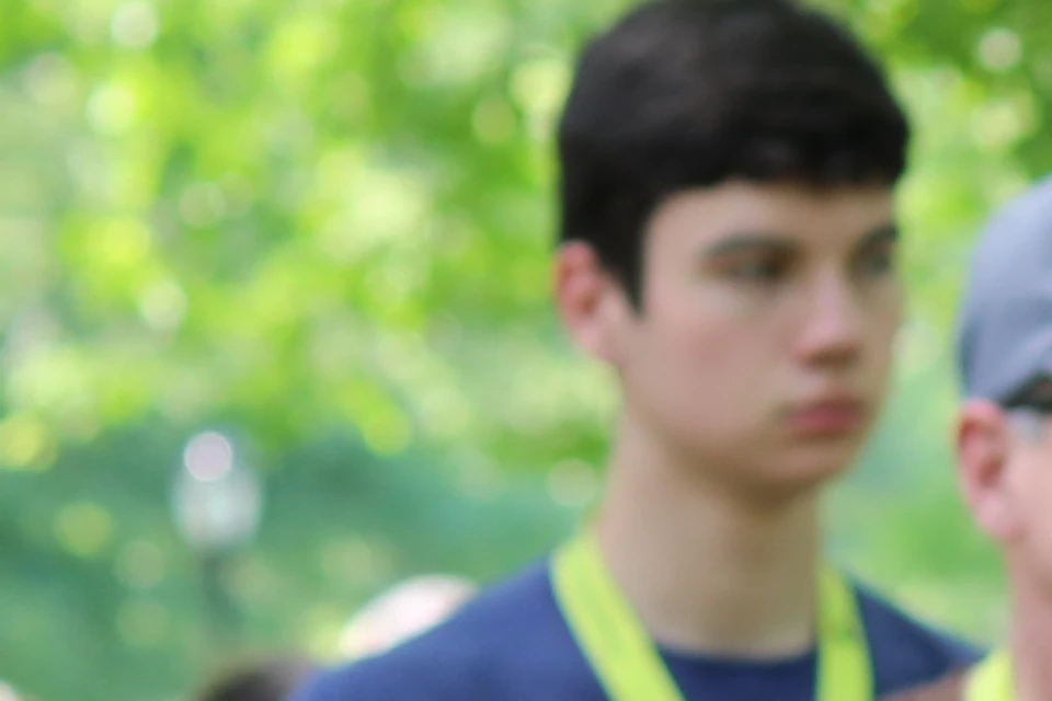 A group of people with green bicycles in a park, listening to a man in a black shirt and cap pointing off-camera.