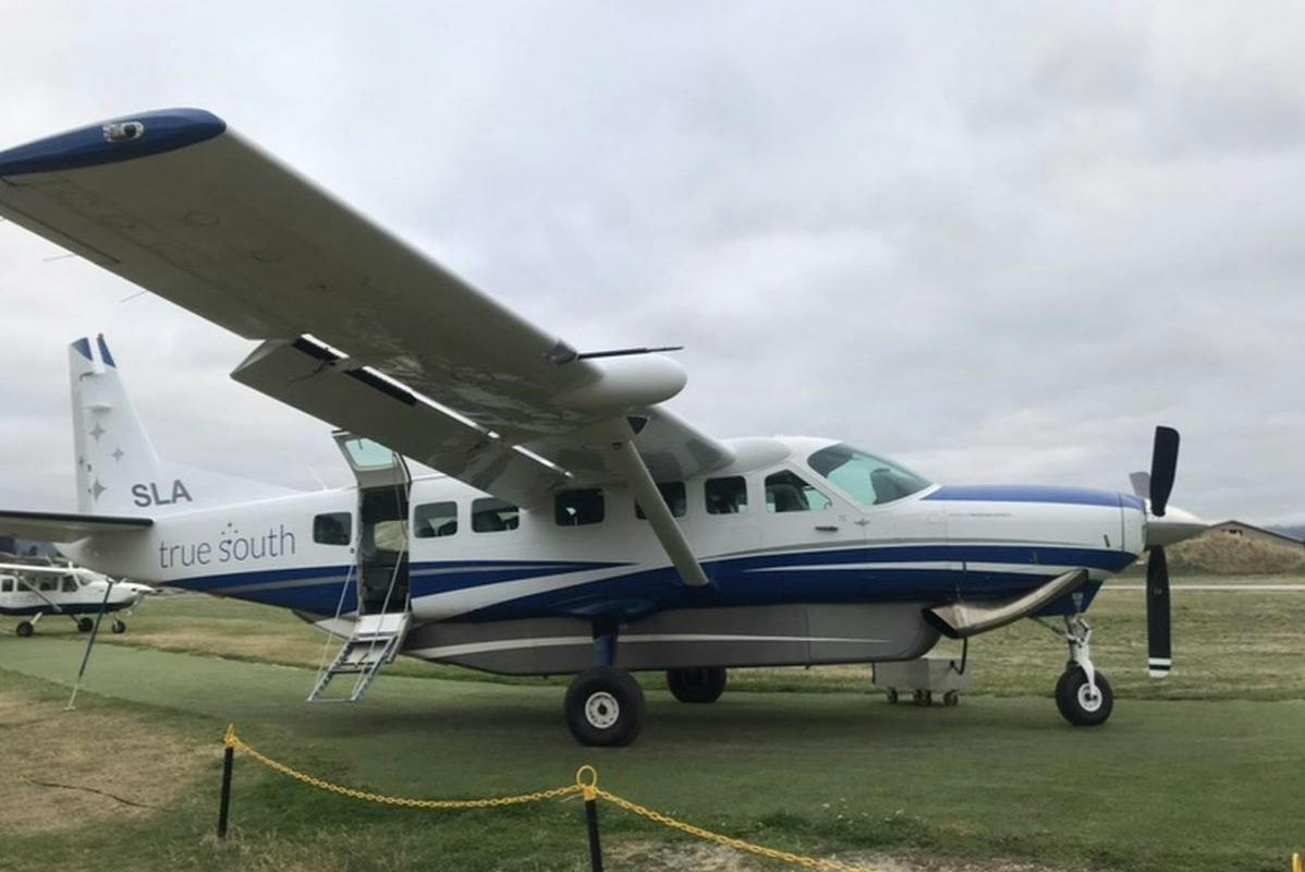 A small white and blue propeller plane parked on a grassy field under a cloudy sky.
