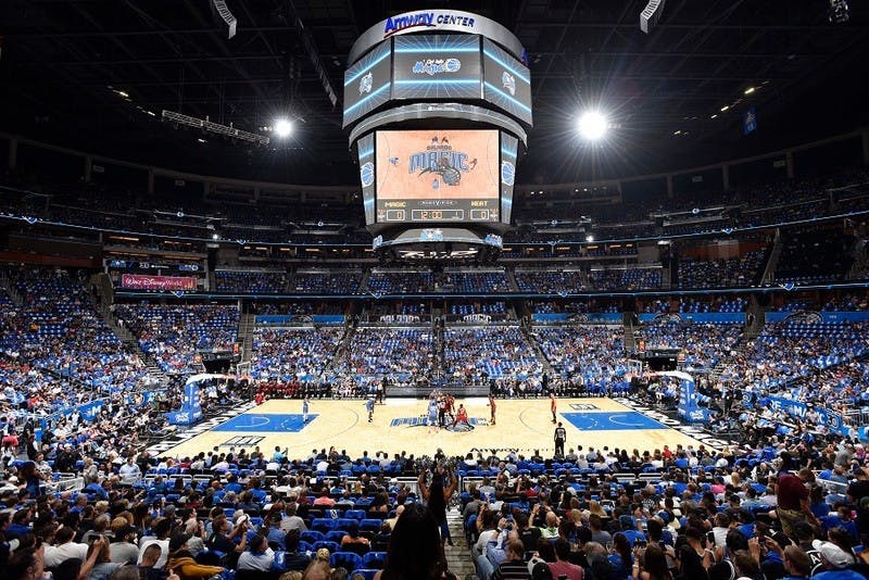 Basketball game at Amway Center, large crowd, players on the court, and a scoreboard overhead displaying "Magic vs. Heat."