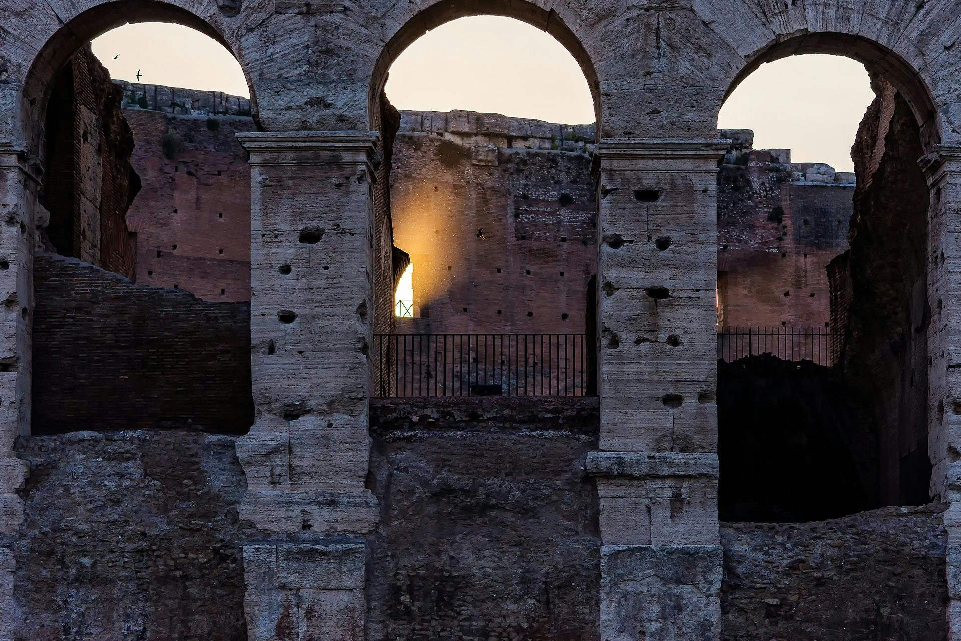 Древнеримские руины с высокими соснами на заднем плане, разбитые колонны, разбросанные по травянистому полю под голубым небом.
