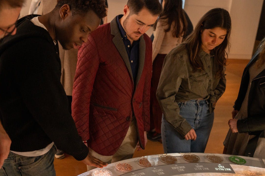 屋内の明るい環境で、さまざまなラベルの付いたセクションがある円形のディスプレイテーブルの周りに立つ人々のグループ。