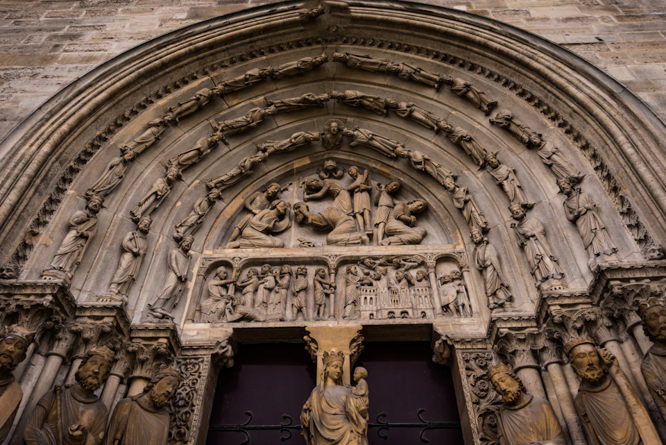 Intricately carved stone archway depicting religious scenes above a doorway adorned with detailed statues.