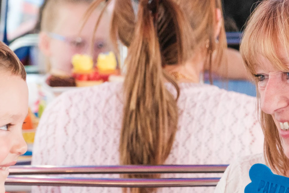 A woman and a boy sit at a table with cupcakes, burgers, and sweets, smiling and holding blue biscuits shaped like bones.