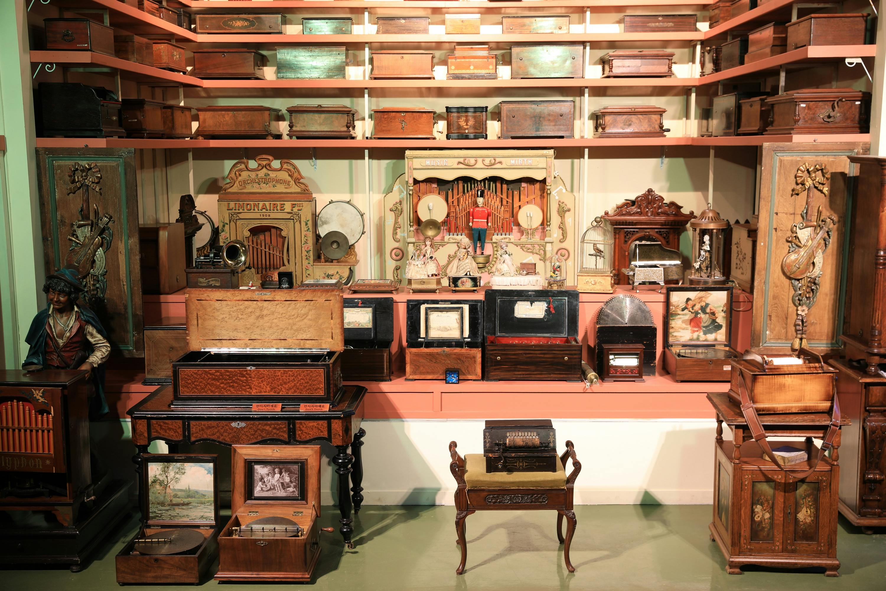 A display of antique music boxes and mechanical instruments on shelves and tables in a well-lit museum setting.