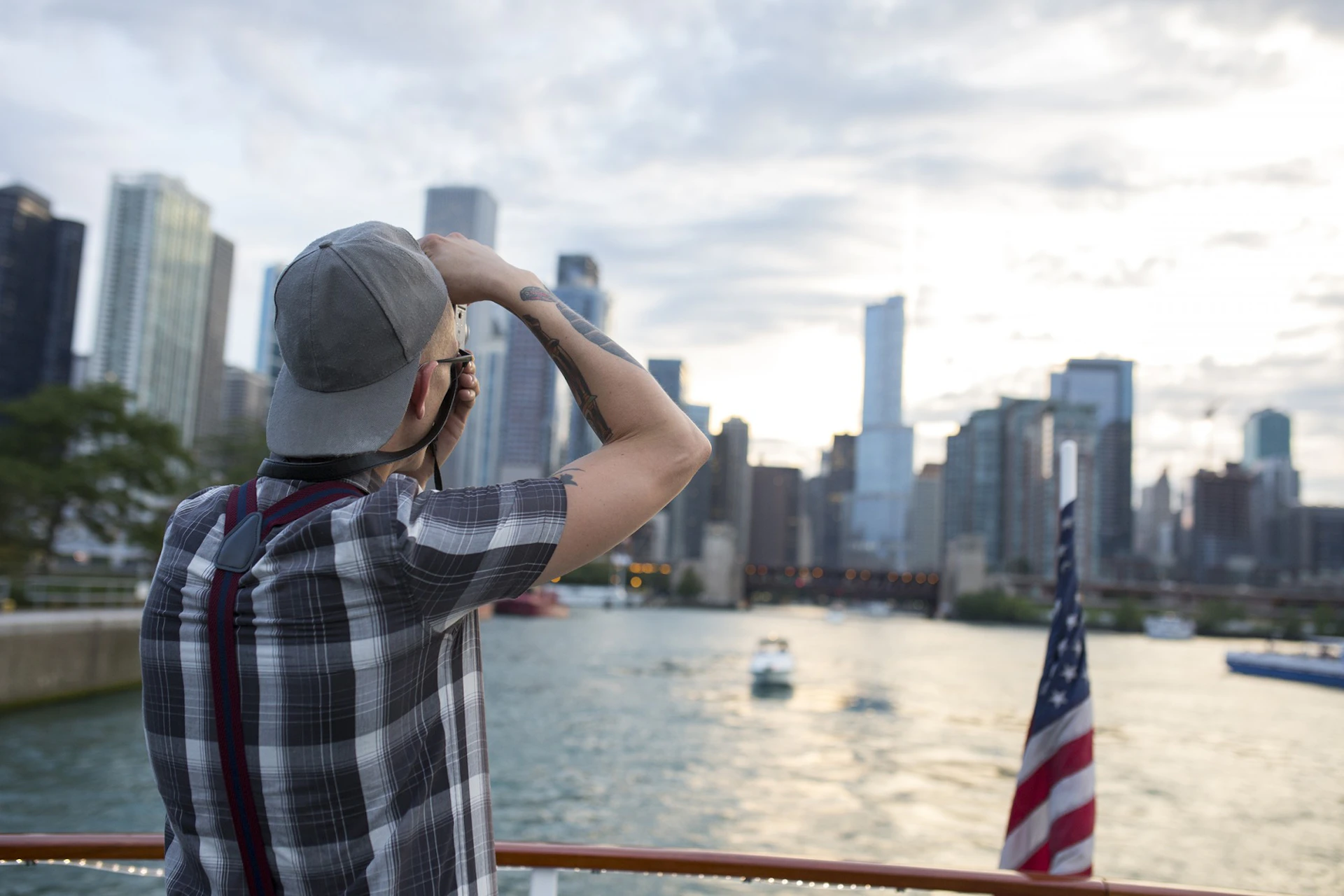 A person on a boat photographs a cityscape with tall buildings; an American flag is on the boat's stern.