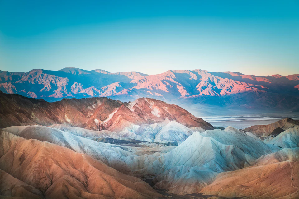 A colorful mountain range under a clear blue sky, showcasing varying hues of red, pink, and white in the rocks.