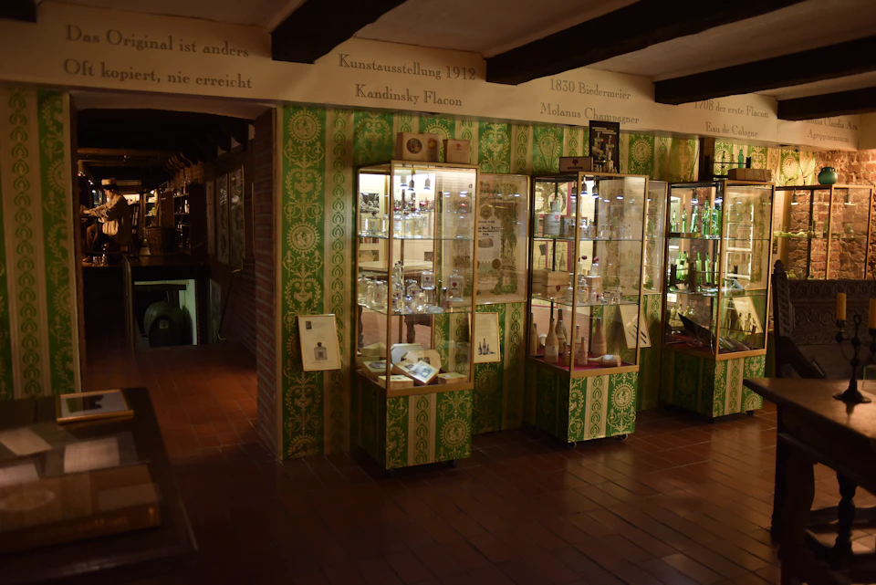 A dimly lit museum with glass display cases filled with various historical objects on a green patterned wall background.
