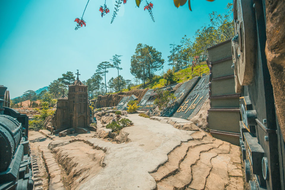 A scenic pathway surrounded by artistic stone structures and lush trees under a clear blue sky.