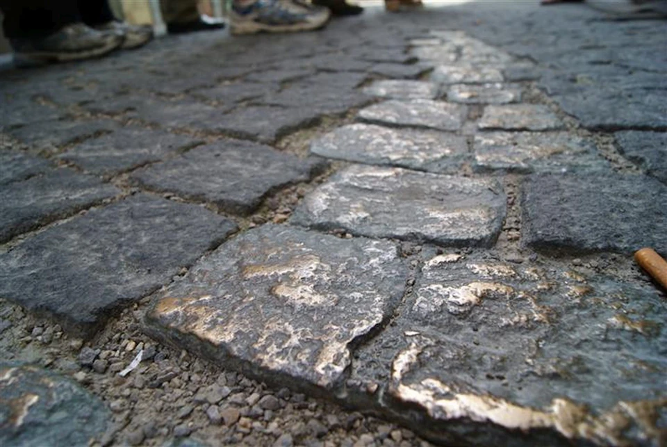 Close-up of worn cobblestones in a paved street, with blurred shoes and legs visible in the background.