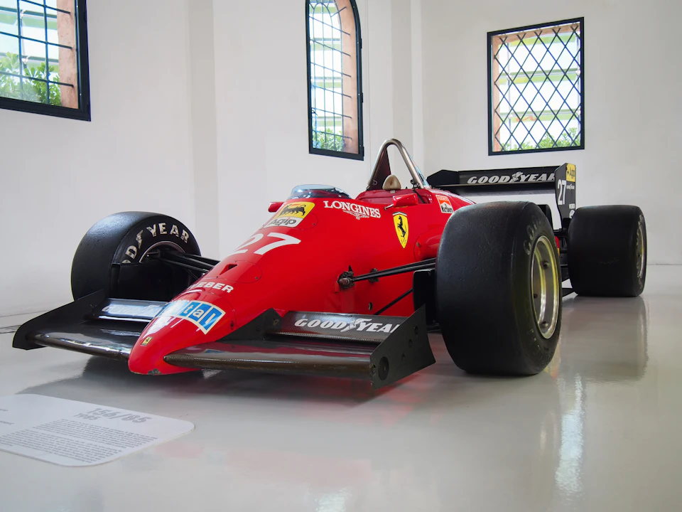 A red Formula 1 race car with Goodyear tires displayed indoors, with large windows in the background.