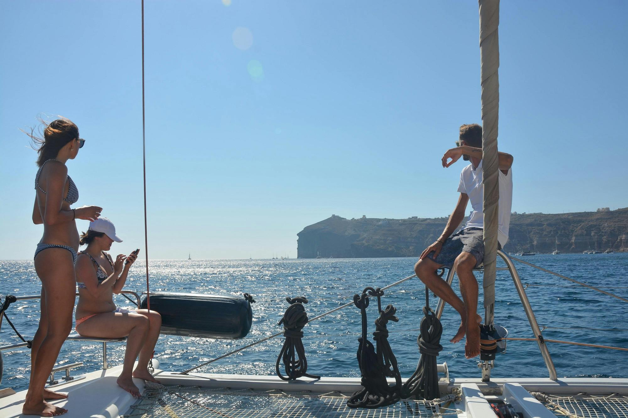 两个人在晴朗的蓝天下在船上放松身心，远处是丘陵海岸线，周围是平静的海面。