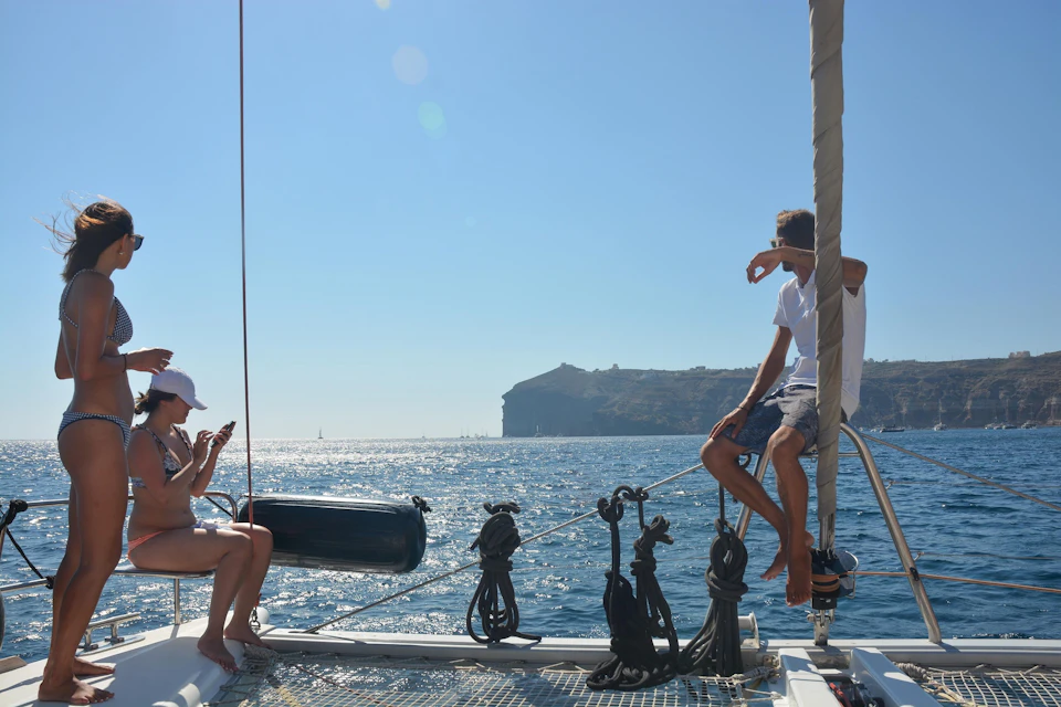 Two people relaxing on a boat under clear blue skies, with a hilly coastline in the distance and calm sea around them.