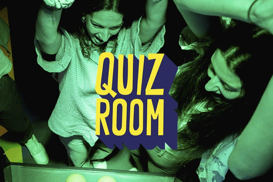 Two people enjoying a game under green lighting, with the text "QUIZ ROOM" prominently displayed over the scene.