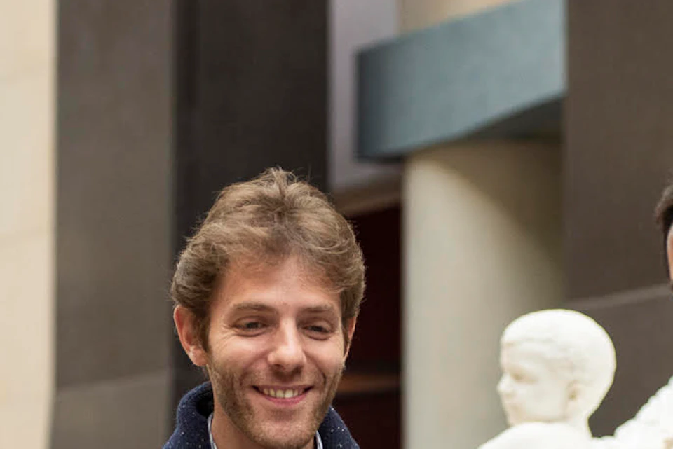 Three people are talking and smiling in an indoor space with classical statues in the background.