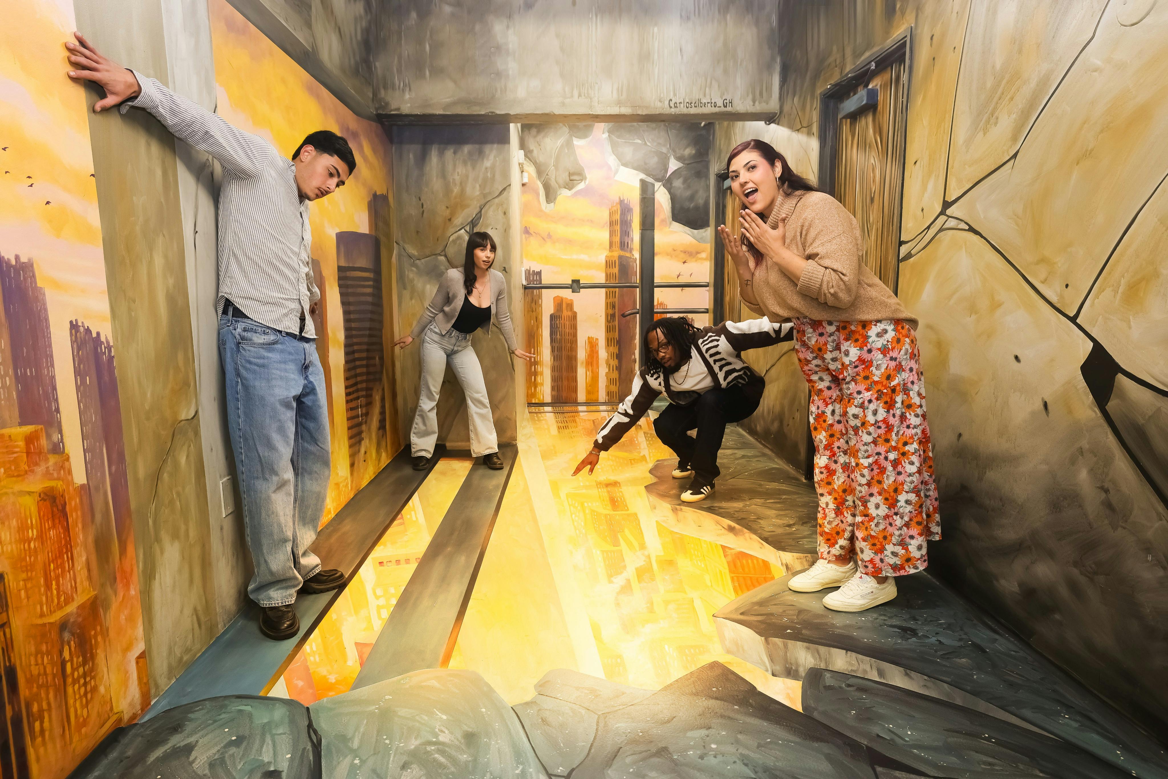 Three people interacting with a perspective-based art installation resembling a cityscape seen through a floor gap.