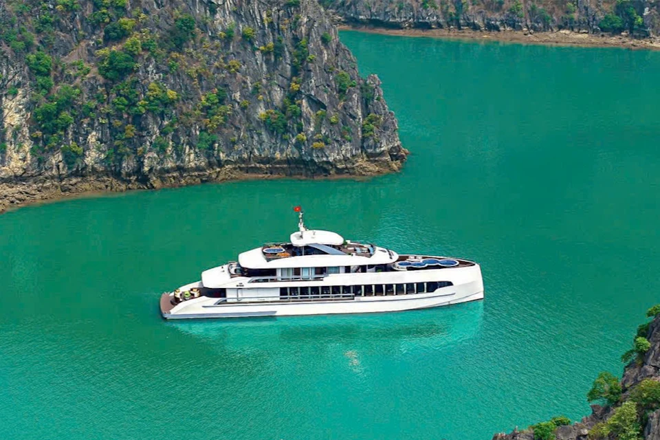 A sleek white yacht floats on turquoise water near rocky, tree-covered cliffs.