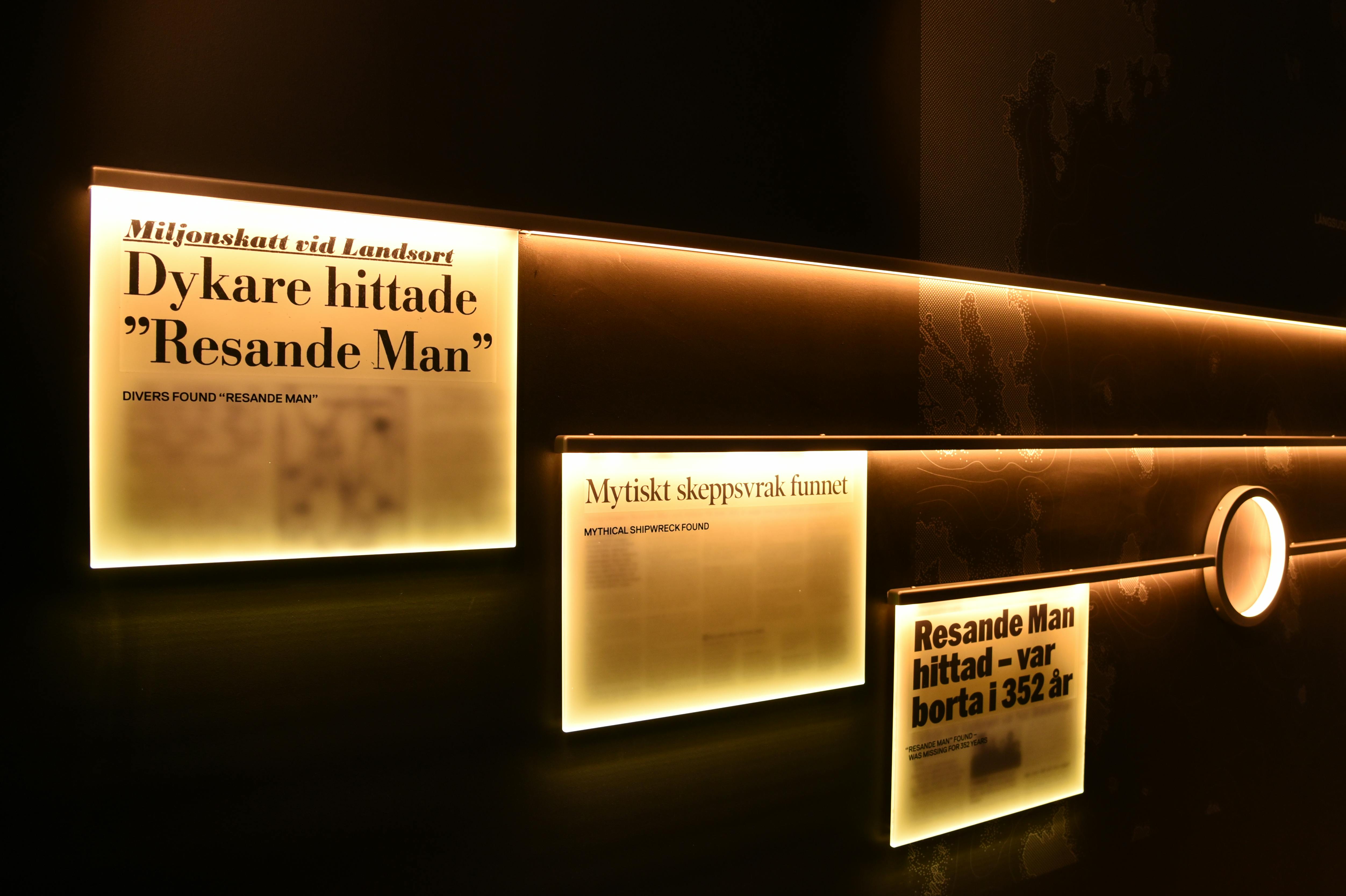 Bakgrundsbelysta displaypaneler med svensk och engelsk text om dykare som hittar skeppsvraket "Resande Man".