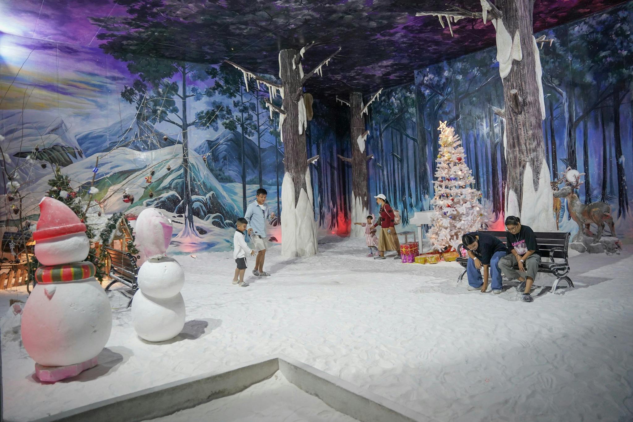 People in a winter-themed indoor setting with artificial snow, a decorated Christmas tree, and forest murals on the walls.