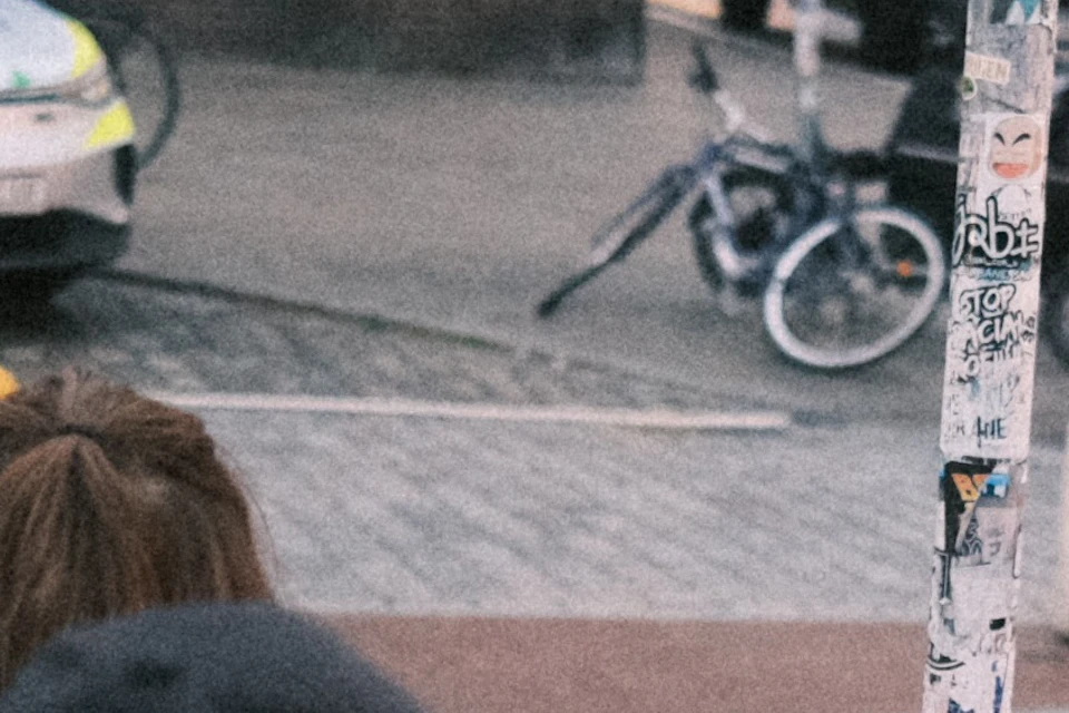 A woman in a pink heart-patterned vest leads a tour group in a bustling urban street with buildings, vehicles, and bikes in the background.