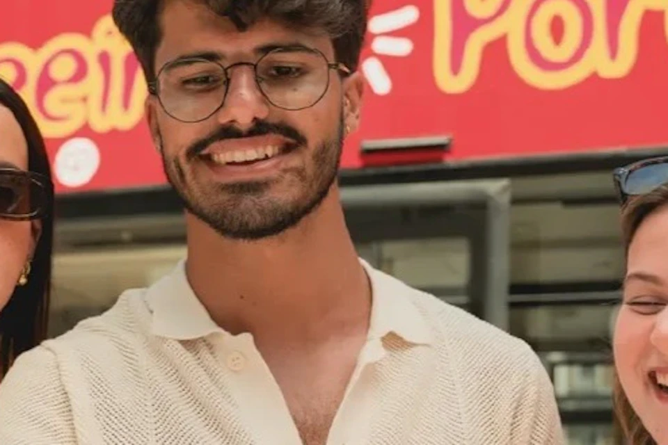 Three people smiling and holding a map in front of a red sightseeing bus with the word 'Portugal' visible on it.