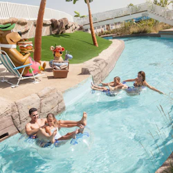 En familj njuter av en lat flodtur i uppblåsbara rör med tecknade figurstatyer och konstgräs på stranden i närheten.