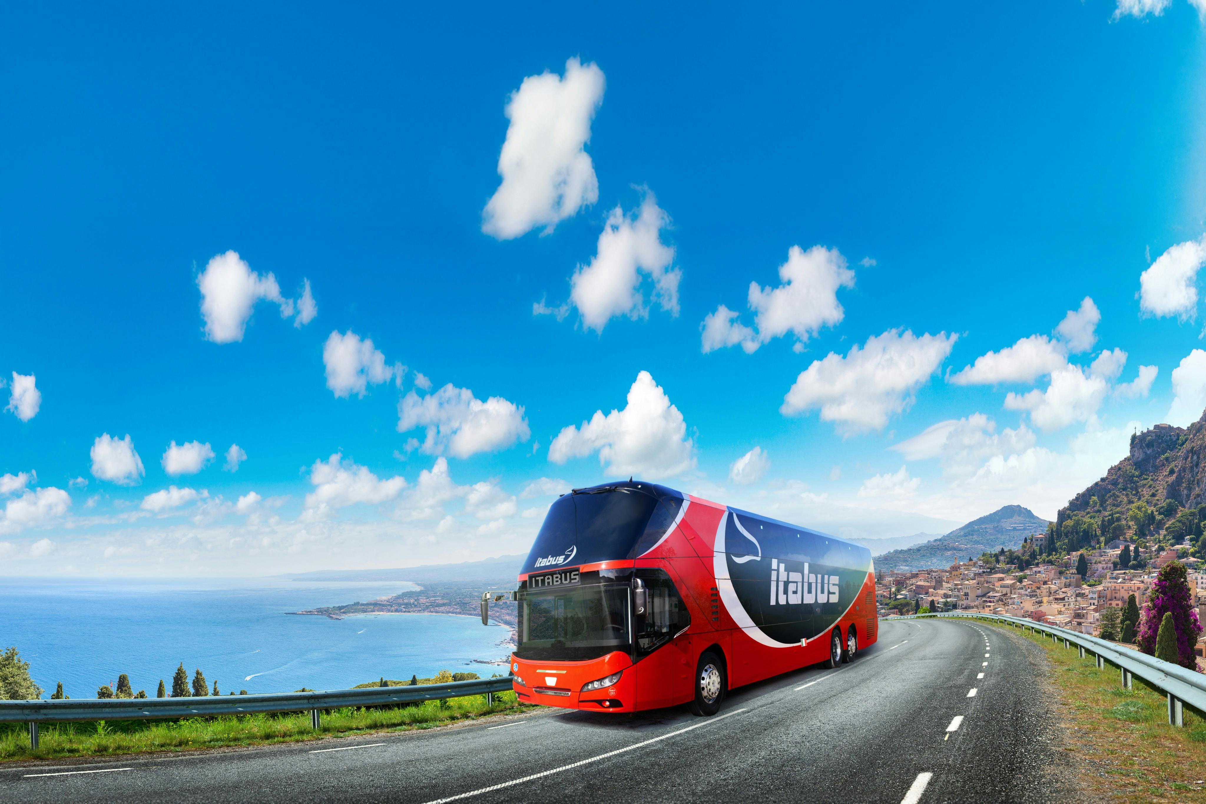 一辆带有「Itabus」品牌的红色和蓝色双层巴士在晴朗的蓝天下沿海高速公路上行驶。