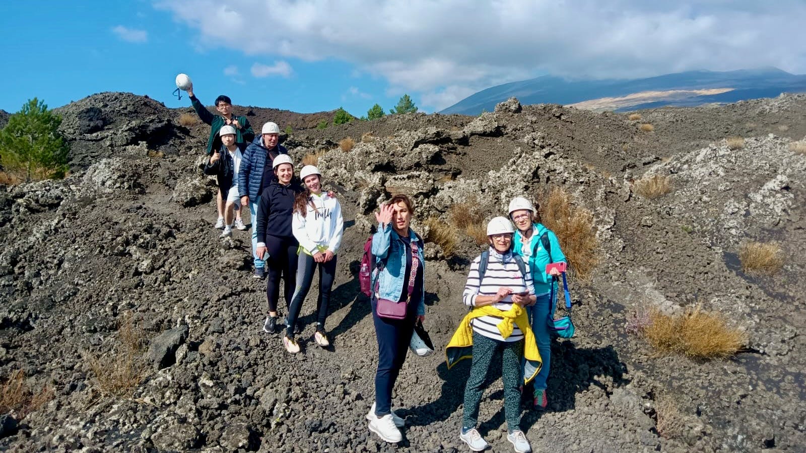 Μια ομάδα επτά ατόμων που φορούν κράνη και ρούχα εξωτερικού χώρου στέκονται σε ένα βραχώδες έδαφος κάτω από έναν εν μέρει συννεφιασμένο ουρανό.