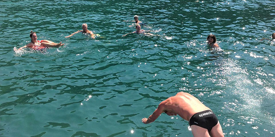 Four people enjoying swimming in a large body of turquoise water, with one person diving in wearing swim shorts.