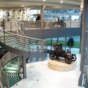 Un museo al coperto con una scala a chiocciola, pareti di vetro, esposizioni di auto d'epoca e veicoli classici su due livelli.