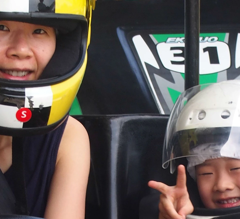 Two people in helmets sitting in go-kart number 33, both making peace signs. Others are visible in the background.