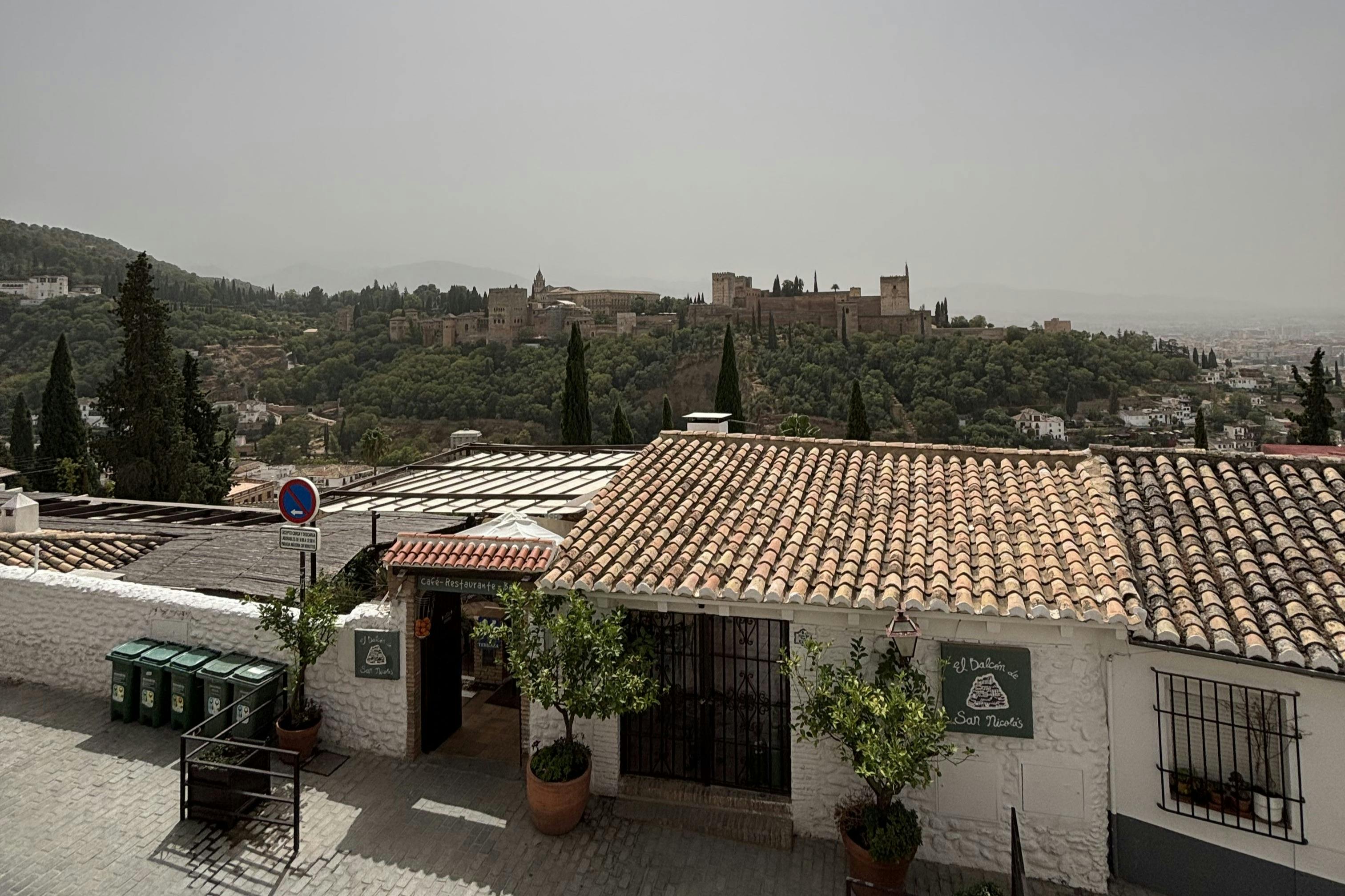 屋顶景观是一栋陶瓦建筑，上面有招牌、盆栽植物和树木覆盖的山丘，后面有一座历史悠久的堡垒。