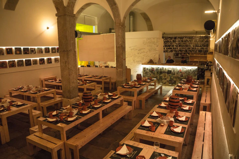 A restaurant with wooden tables and benches, set with plates and mugs. Walls are decorated with photos and handwritten messages.