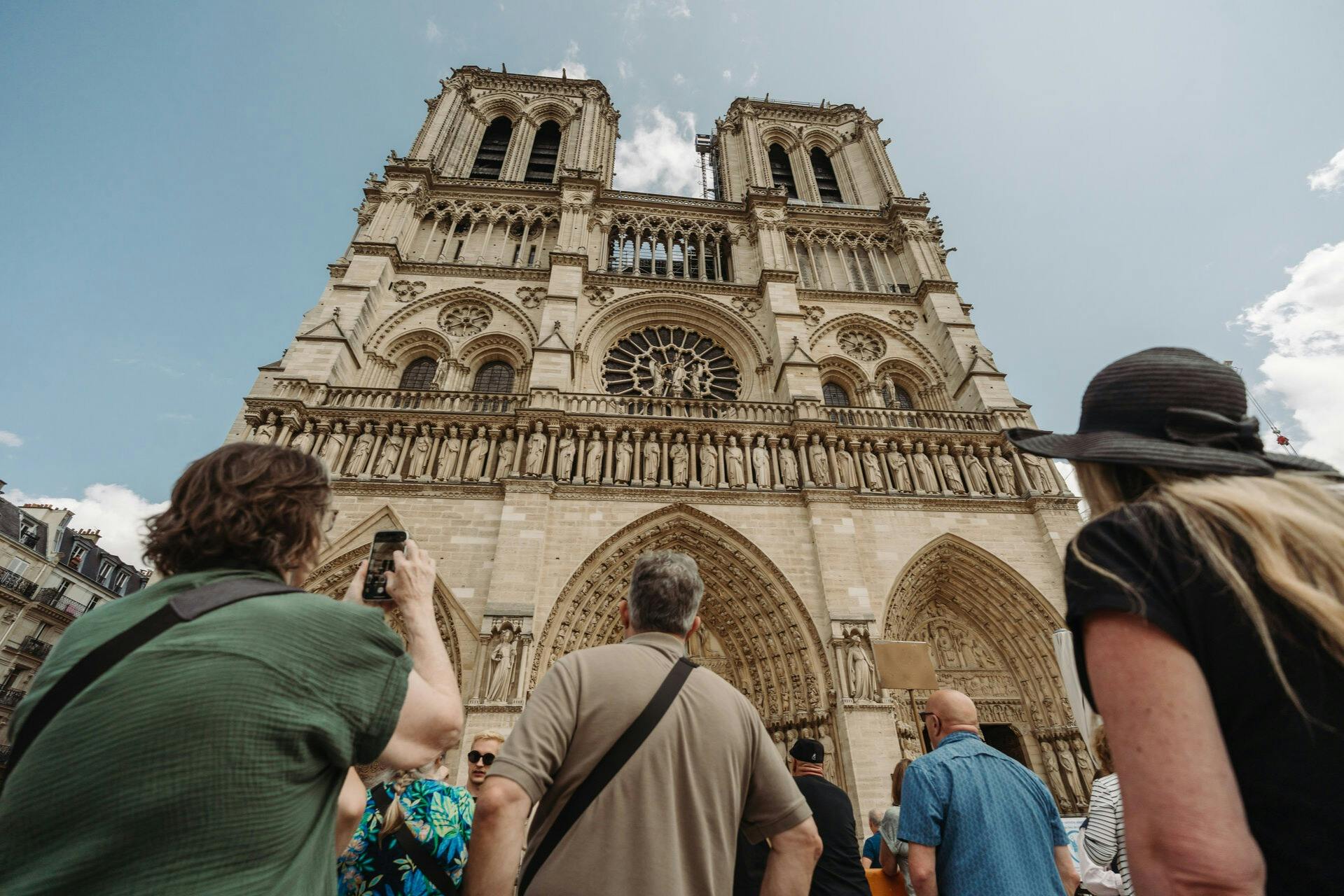 People standing in front of the Notre-Dame Cathedral, looking up at its gothic facade under a clear sky.