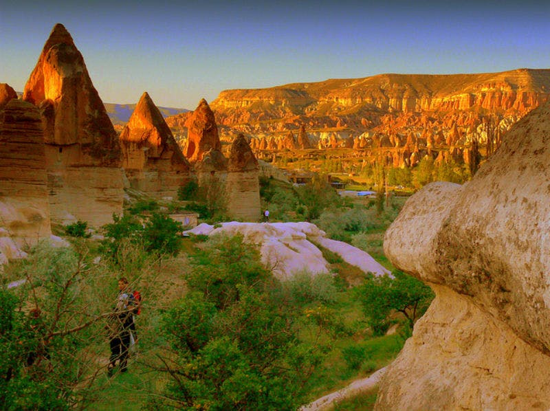 Rock formations and greenery in a valley at sunset, with two people exploring the area.