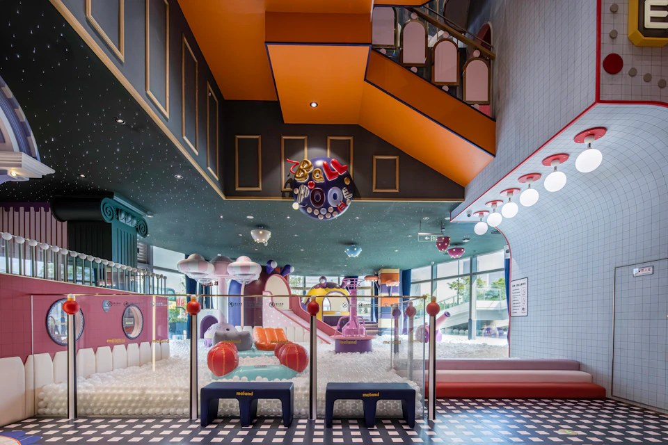 A colorful indoor children's play area with slides, ball pits, and vibrant decor under a high ceiling with lights.