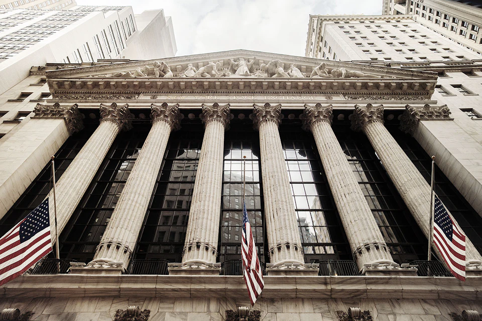 Facade of a historic building with tall columns and an American flag, surrounded by modern skyscrapers.