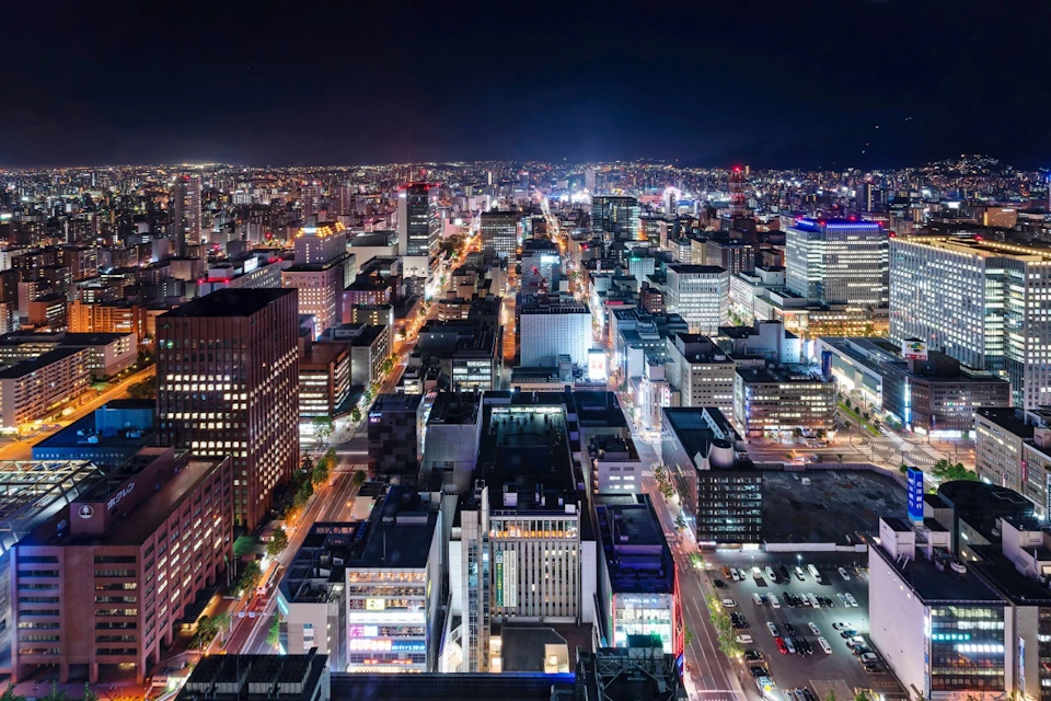 Aerial view of a bustling cityscape at night with illuminated buildings, streets, and vehicles.