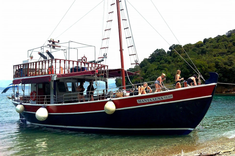 A red and black boat with people sunbathing and relaxing, moored near a forested shoreline.