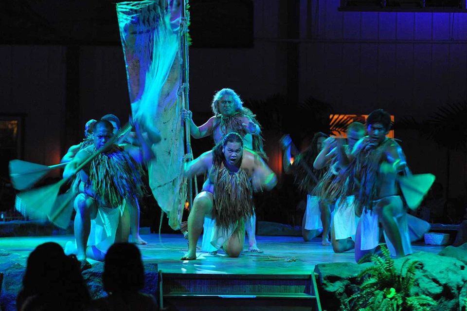 Performers in traditional attire dance energetically on stage with vibrant blue and green lighting in the background.