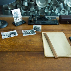 Skrivbord med vintagefoton, papper, en linjal, en lampa, en brevhållare, ett svart marmorbläckhus, en låda och en filmapp.