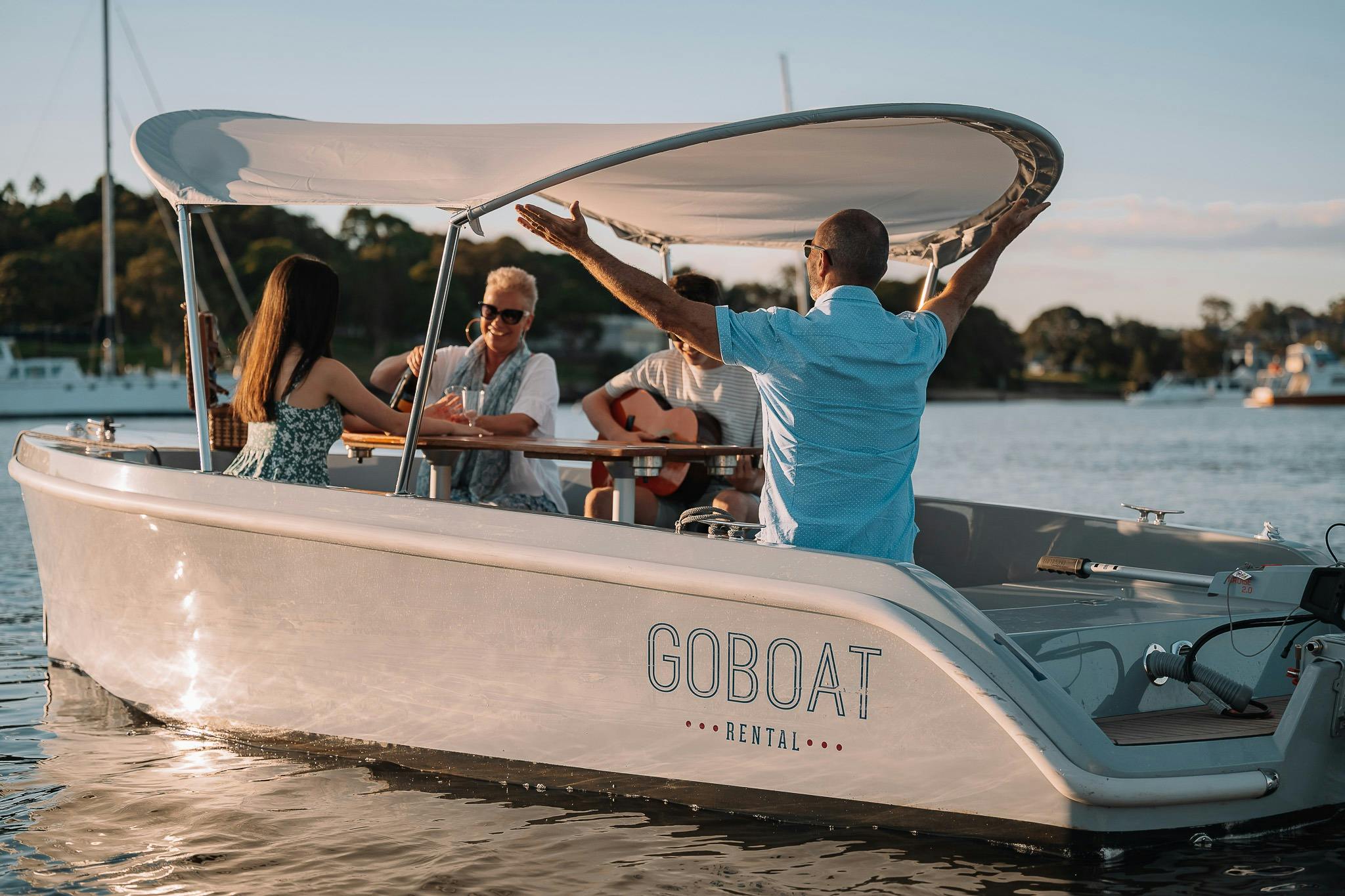 GoBoat żeglujący z czterema gośćmi na pokładzie, którzy dzielą się historiami przy butelce wina