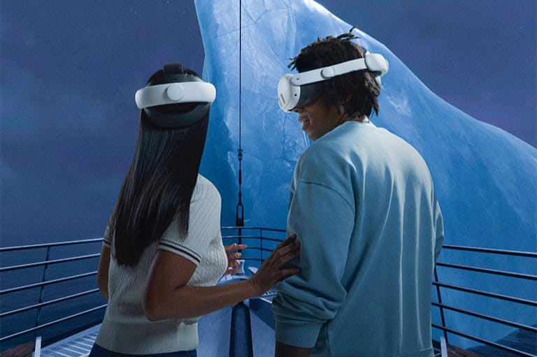 Two people wearing VR headsets stand on a platform, facing a large iceberg in the background.