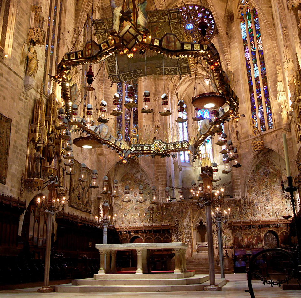 Elaborate cathedral interior with stained glass windows, large ornamental chandeliers, an altar, and intricate wall carvings.