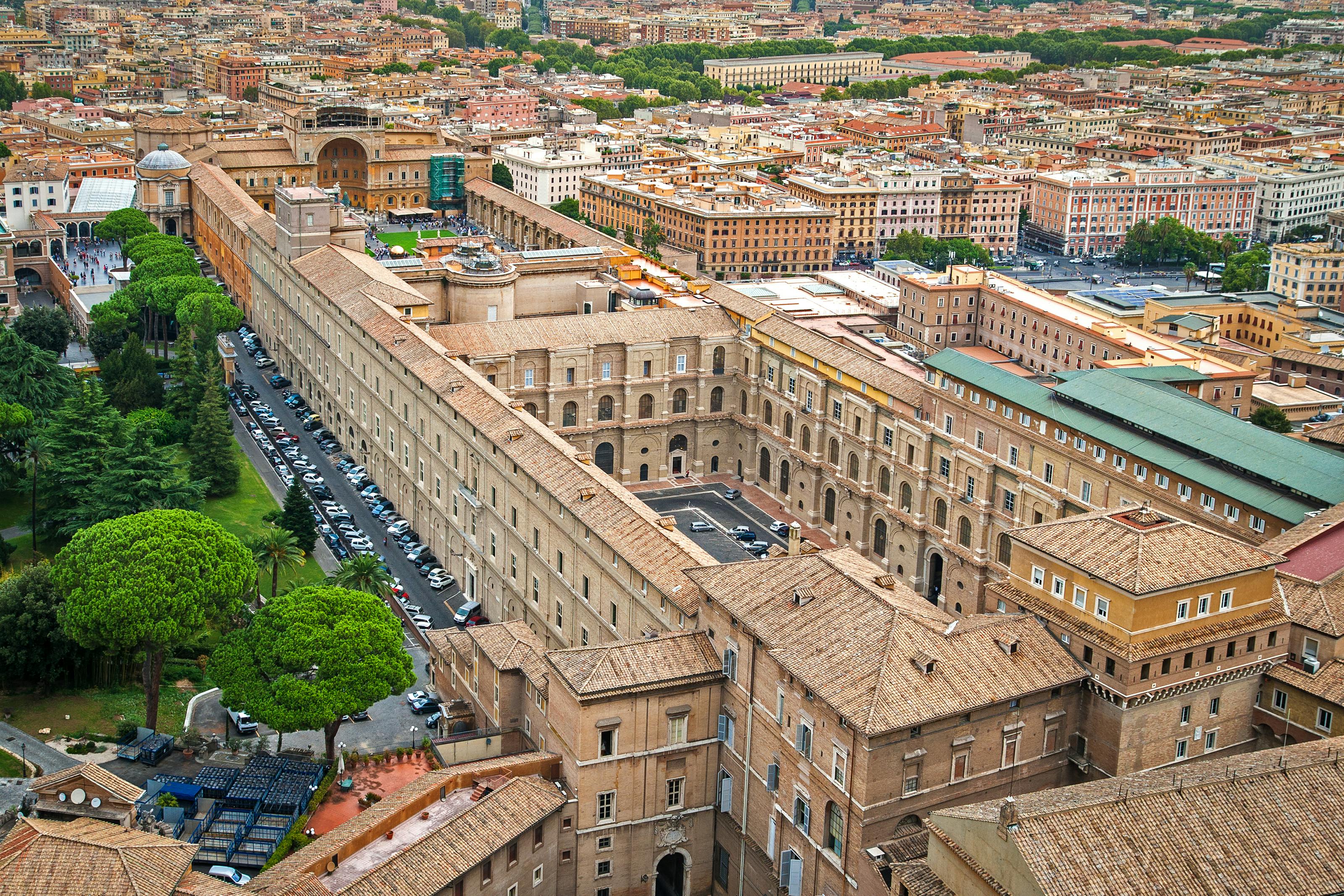 Aerial view of a large, historic, rectangular building complex in an urban area with many surrounding buildings and green spaces.