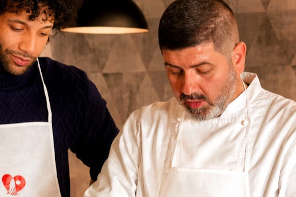 A chef teaches three people how to knead dough on a marble countertop in a cooking class setting.