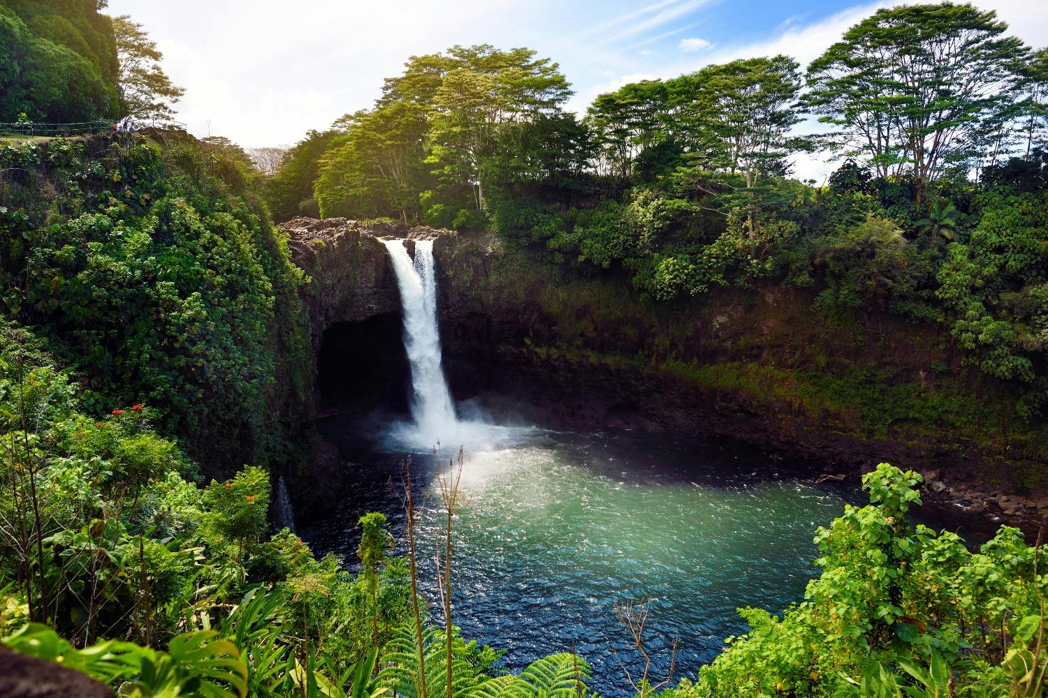 A scenic view of a waterfall cascading into a calm pool surrounded by lush greenery under a clear blue sky.